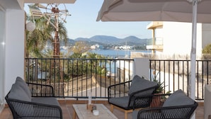A balcony with wicker furniture, a table, and a view of a body of water and mountains. - Hotel Es Mitjorn (Sant Antoni de Portmany)