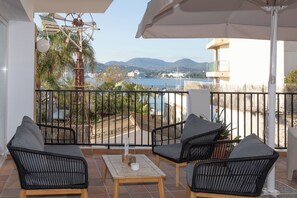 Un balcón con mobiliario de mimbre, una mesa y vistas al agua y a las montañas.