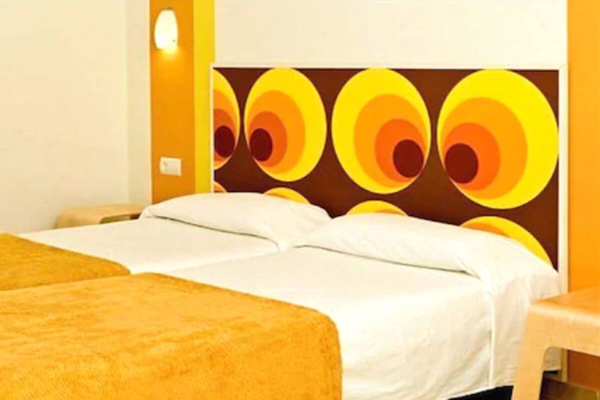 A hotel room with two beds, a large wall mural, and a small table.