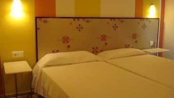 A hotel room with two beds, a headboard with floral patterns, and bedside lamps.