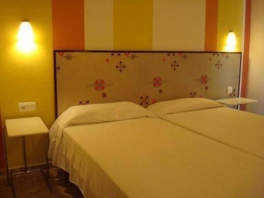 A hotel room with two beds, a headboard with floral patterns, and bedside lamps.