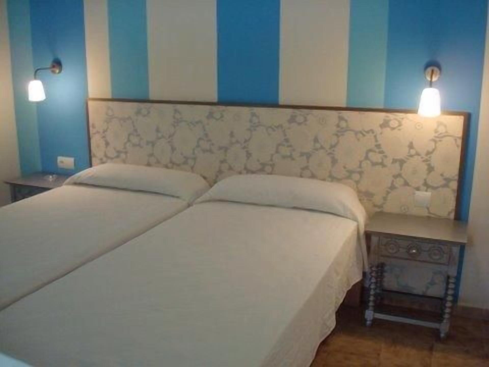 A double bed with a patterned headboard, bedside tables with lamps, and a blue and white striped wall.