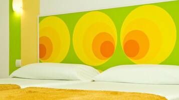 Habitación de hotel con una cama, almohadas blancas y una pared verde con un diseño circular.