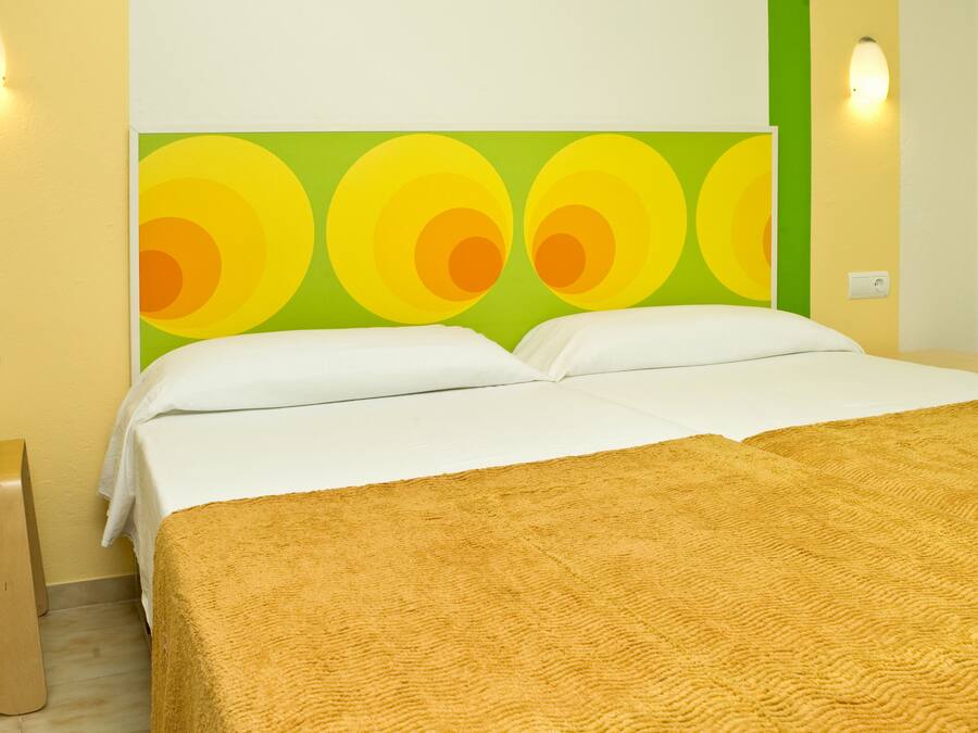 Una camera d'albergo con un letto, pareti verdi e un'ampia opera d'arte circolare sopra il letto.