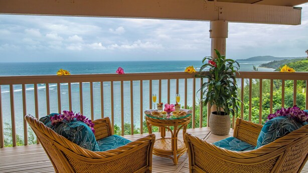A balcony with wicker furniture and a glass table, overlooking a coastal view. - Club Wyndham Shearwater (Princeville)