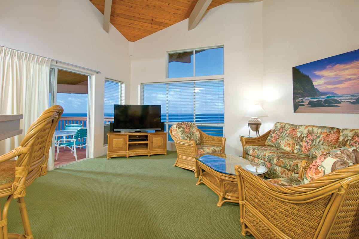 A living room with wicker furniture, a flat-screen TV, and a painting of a beach scene.