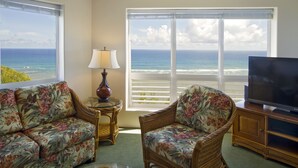 A living room with a view of the ocean, a sofa, a chair, a lamp, and a television. - Club Wyndham Shearwater (Princeville)