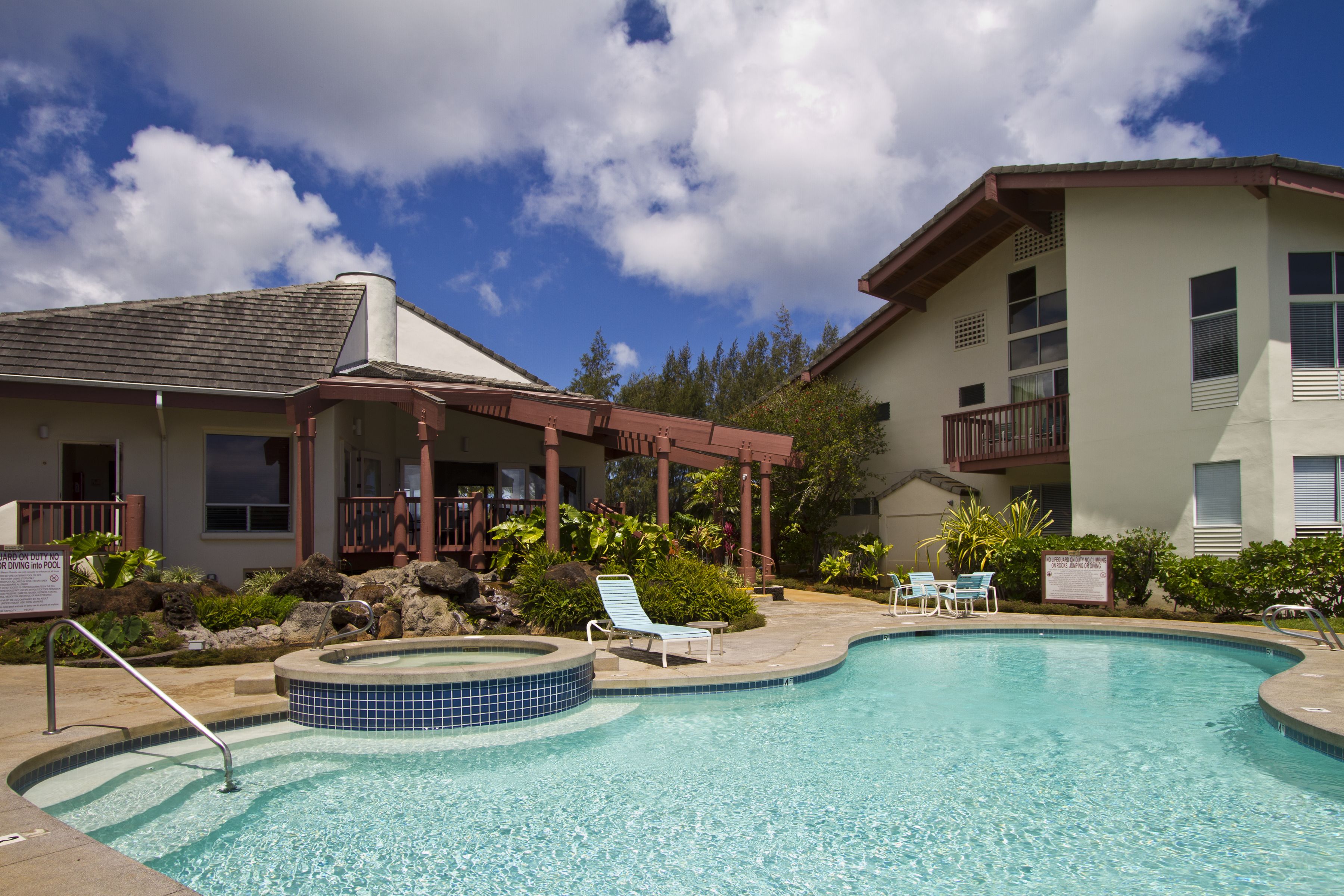 Une piscine avec des chaises longues, un jacuzzi et un bâtiment doté d’un balcon.