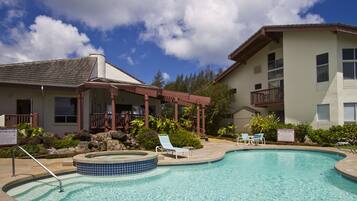 Une piscine avec des chaises longues, un jacuzzi et un bâtiment doté d’un balcon.