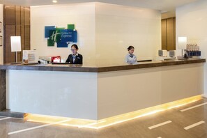 A hotel reception desk with two staff members, a digital display, and a sign for Holiday Inn Express. - Holiday Inn Express Xi'an High-tech Zone by IHG (Xi'an)