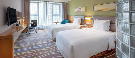 A hotel room with two beds, a desk, a TV, and a window with curtains.