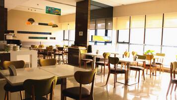 A spacious dining area with multiple tables and chairs, a kitchen area with a stove, and large windows allowing natural light.