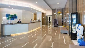 Zona de recepción de hotel con diseño moderno, que incluye un mostrador de recepción, un área de estar y una exhibición de servicios.