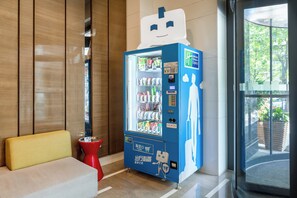 A blue vending machine with a cartoon character, located in a modern lobby with wooden paneling and a yellow bench. - Holiday Inn Express Xi'an High-tech Zone by IHG (Xi'an)