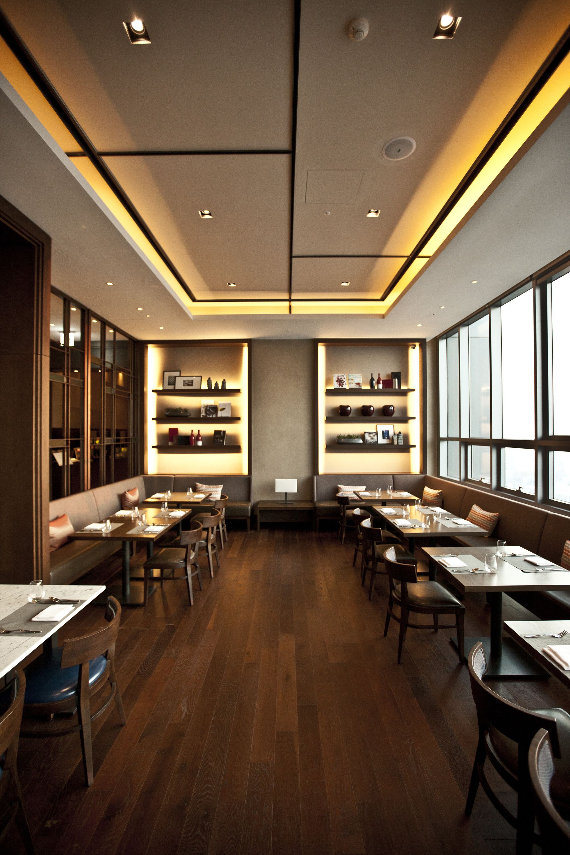 A restaurant with wooden flooring, tables, and booths, featuring shelves with decorative items and a large window on one side.