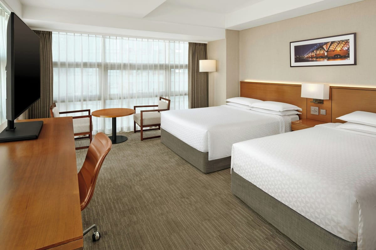 A hotel room with two beds, a desk, a chair, a TV, and a large window with curtains.