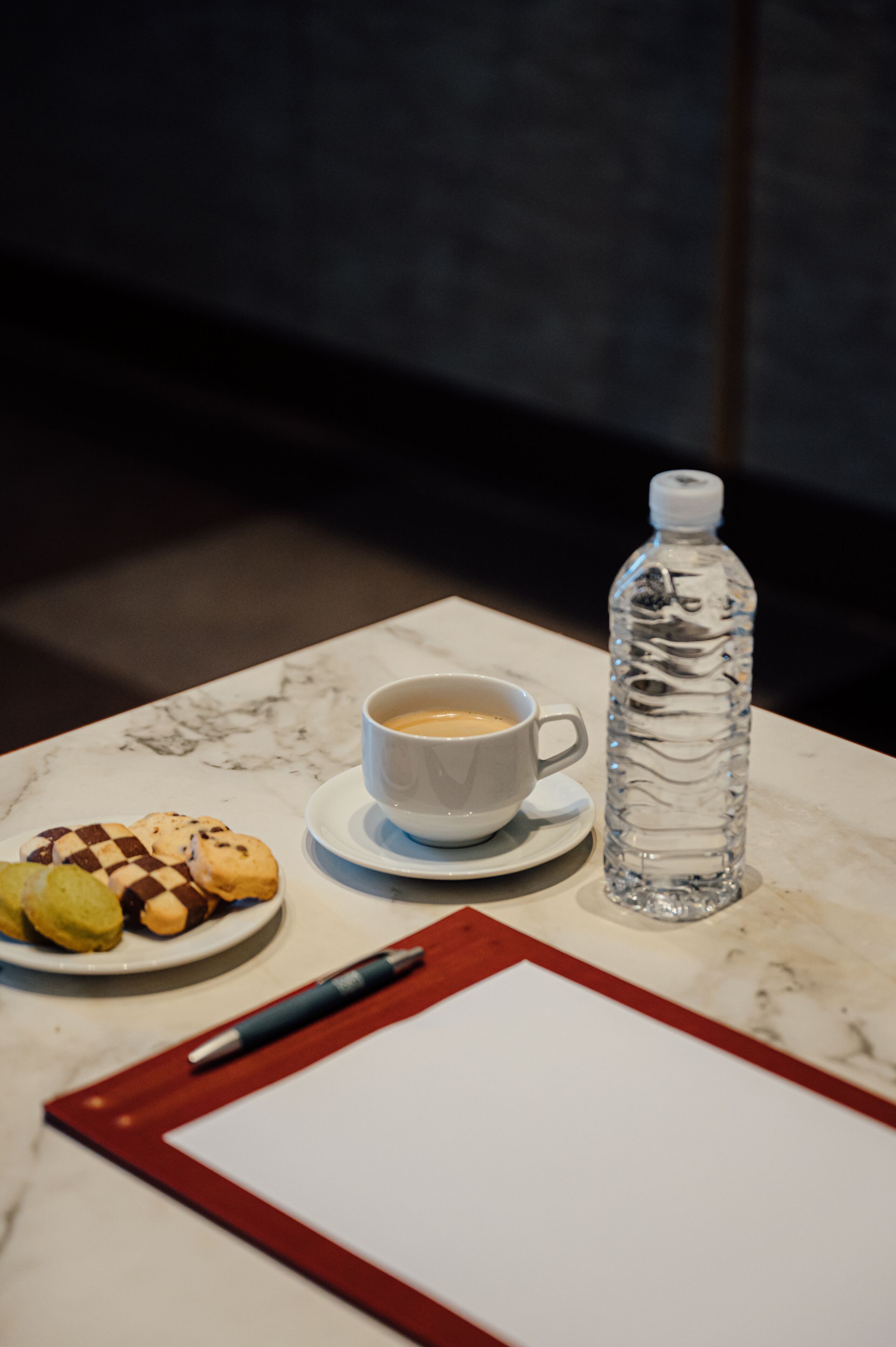 A table with a cup of coffee, a bottle of water, a plate of cookies, a pen, and a notepad.
