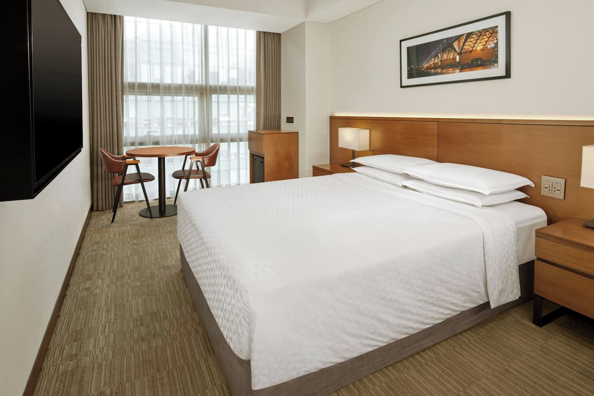 A hotel room with a large bed, a desk with a chair, a TV, and a window with curtains.