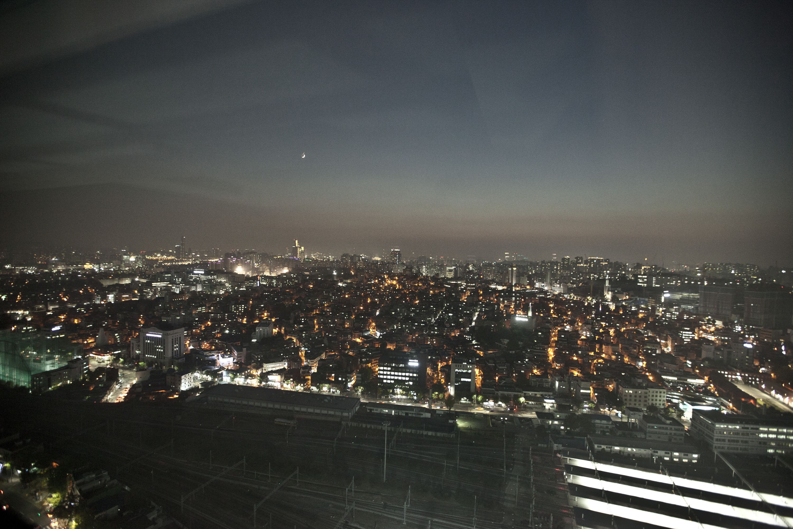 A nighttime cityscape with illuminated buildings and a distant moon.