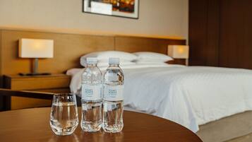 A hotel room with a neatly made bed, two bedside lamps, and three bottles of water on a wooden table.