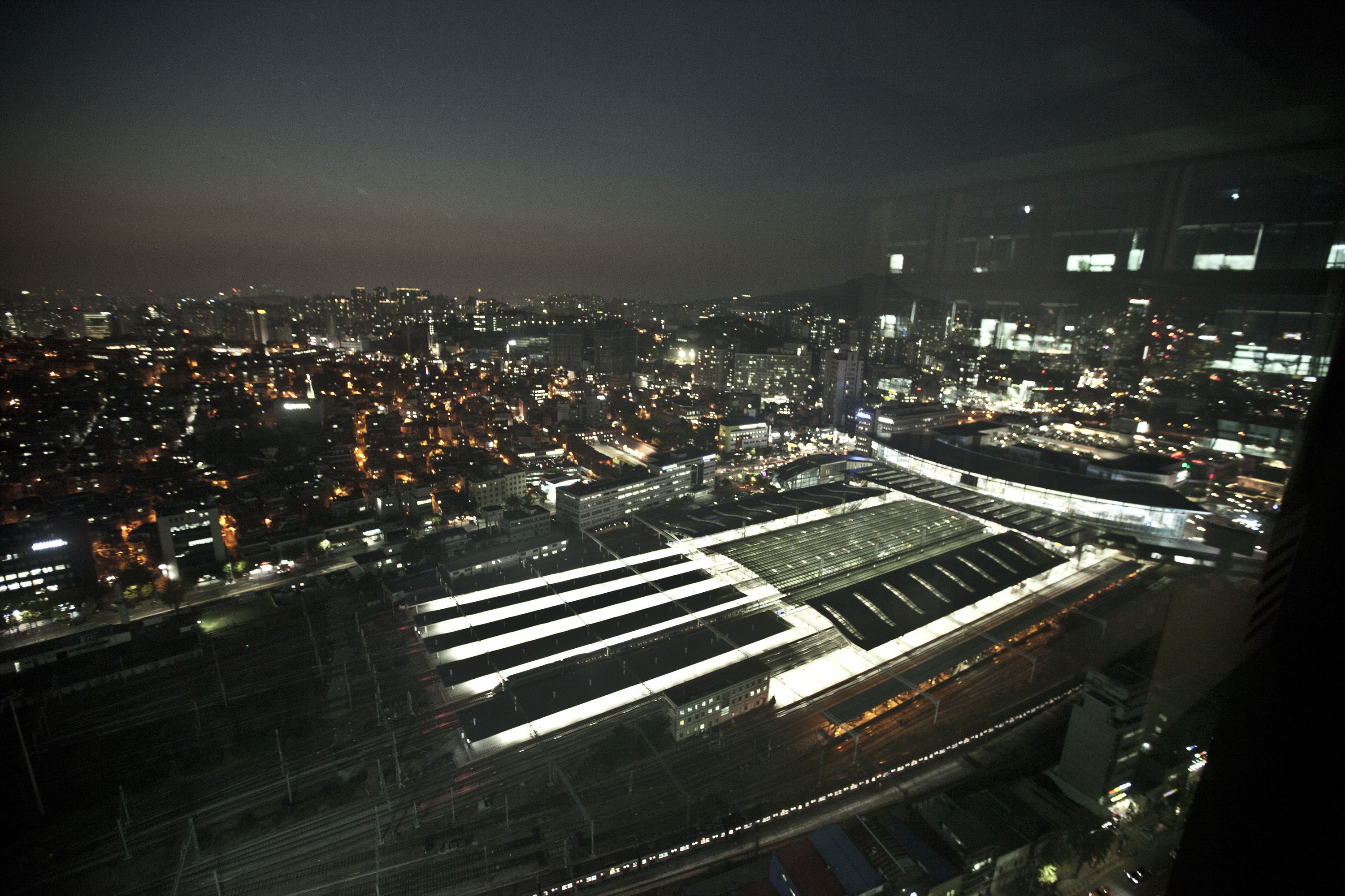 A nighttime cityscape with a large, illuminated train station and surrounding urban area.