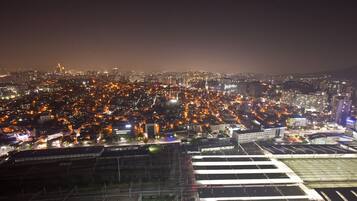 Paisagem urbana noturna com edifícios iluminados e uma área ampla, com estruturas que parecem fazer parte de um centro de transporte.
