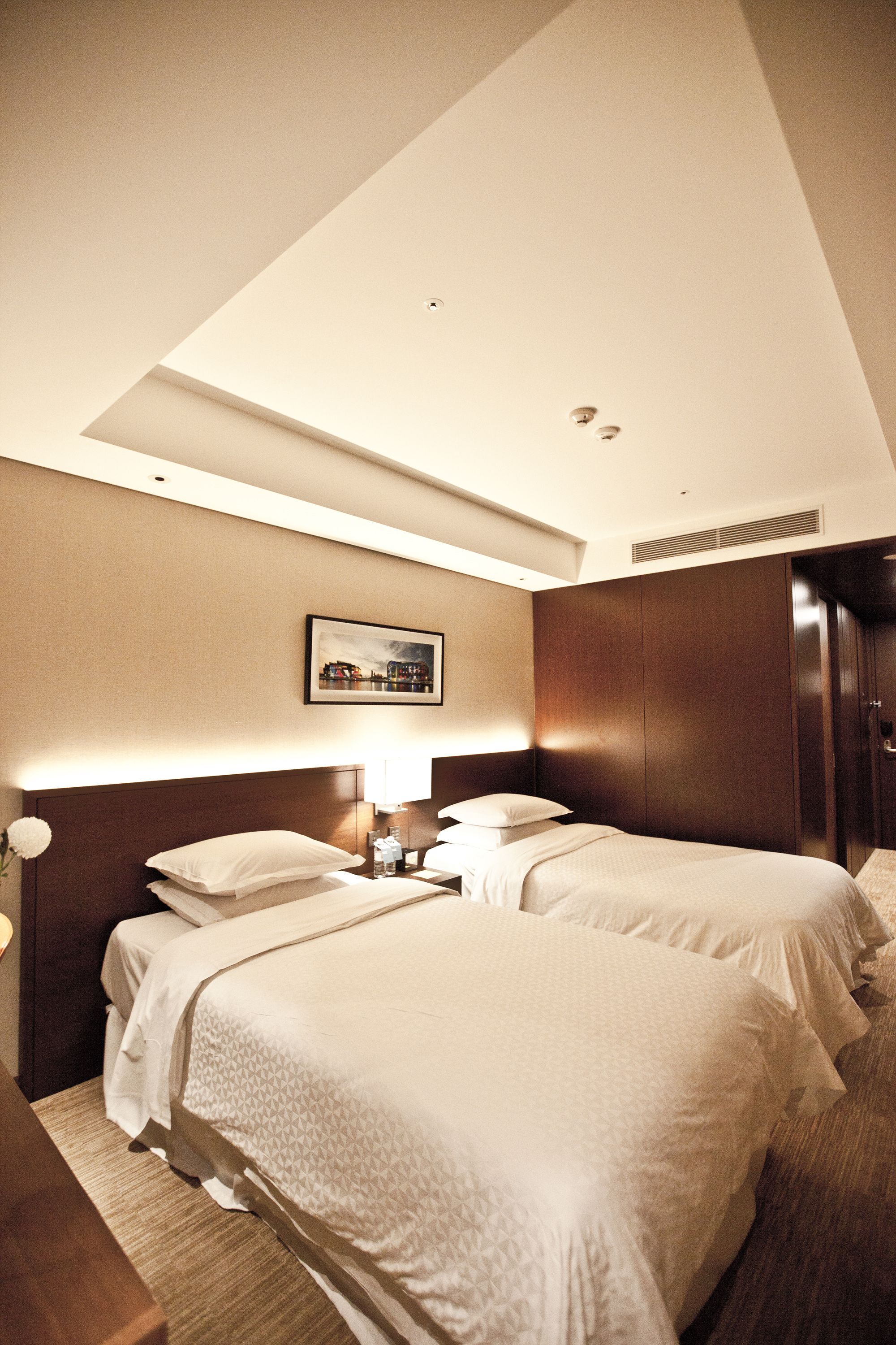 A hotel room with two beds, a large framed picture on the wall, and a wardrobe.