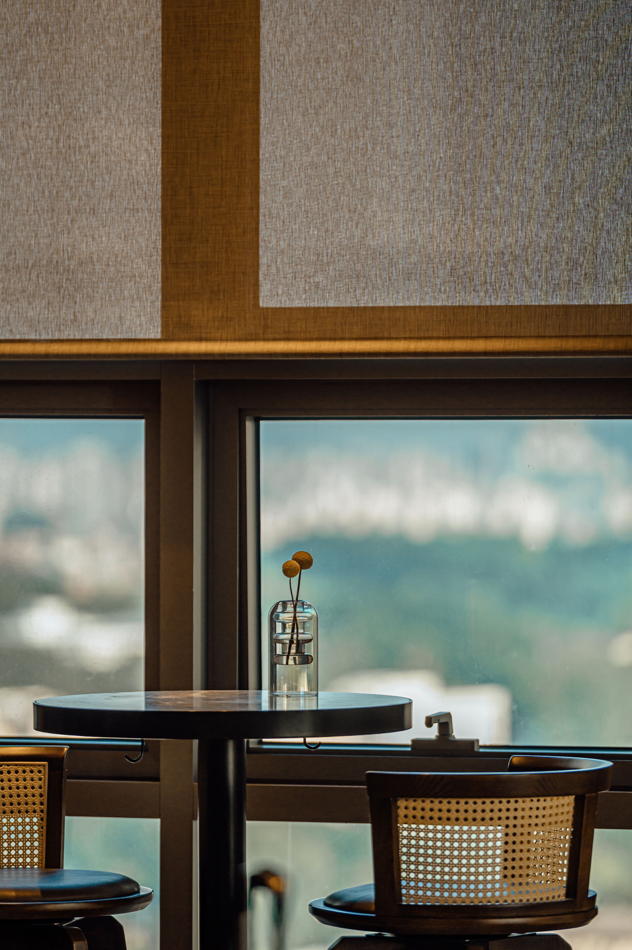 Un comedor con una mesa y sillas, una ventana con vistas al cielo y un florero con una flor sobre la mesa.