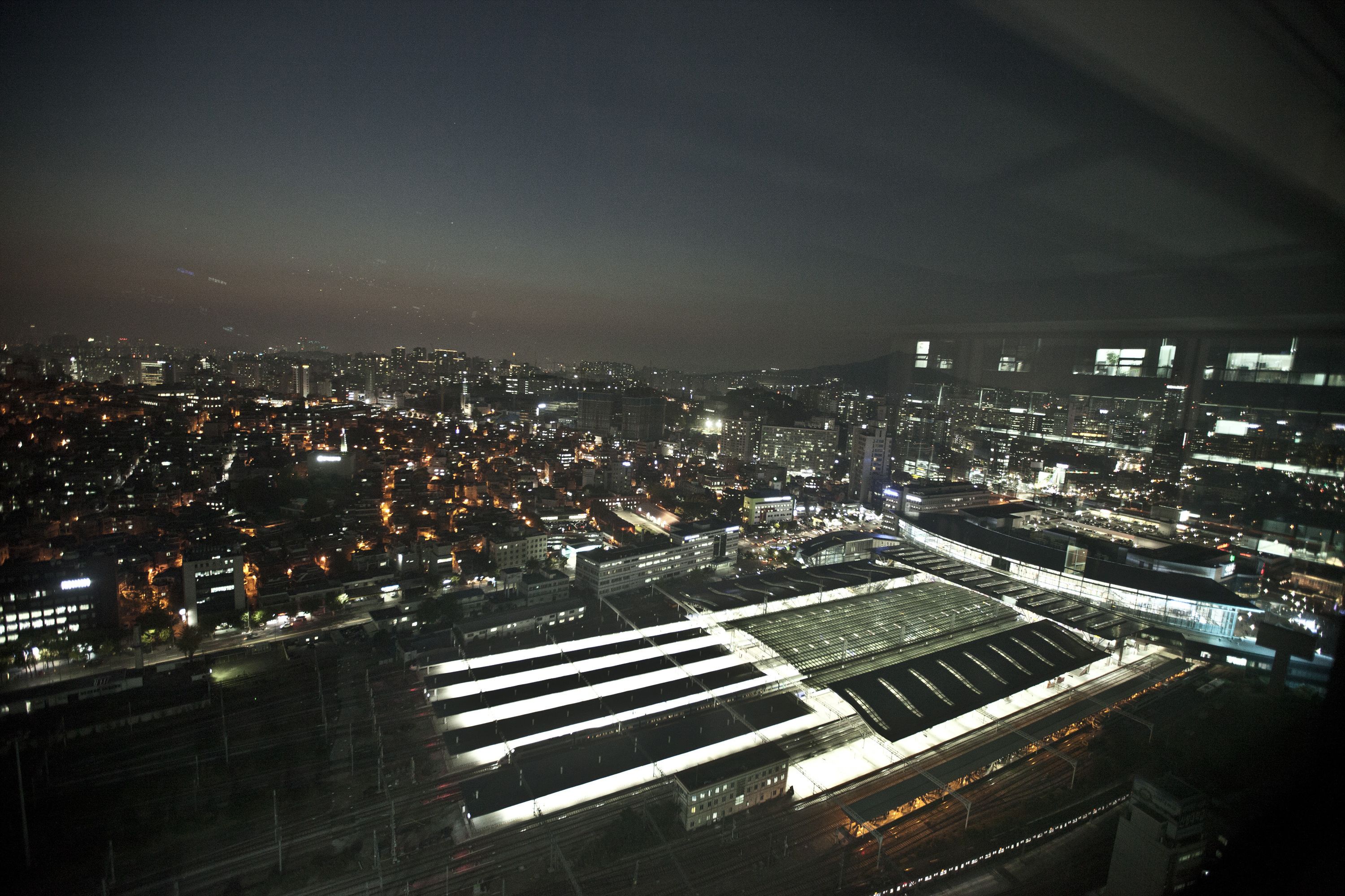 An aerial view of a city at night with illuminated buildings and a large, well-lit train station.
