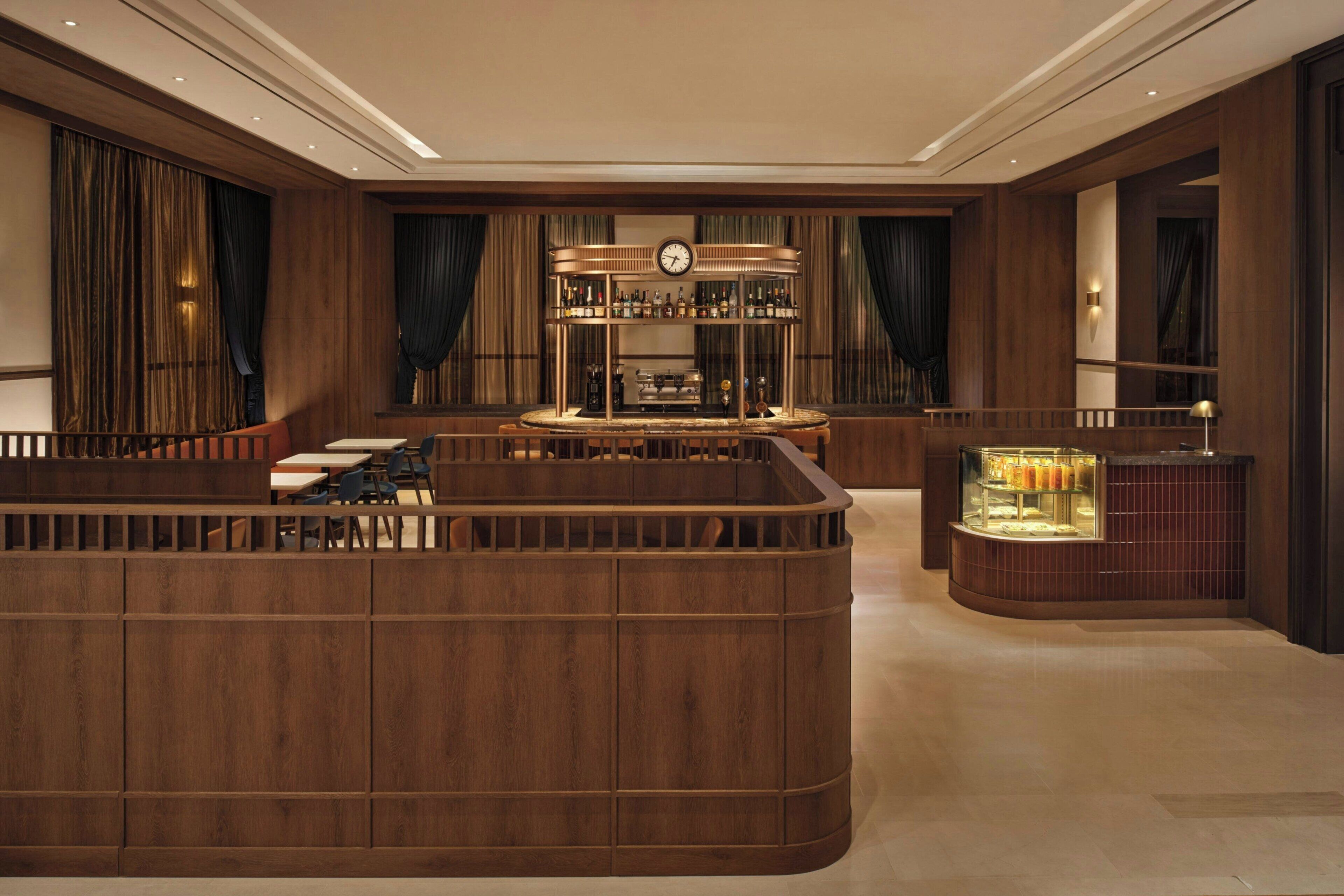 Uma área de bar com relógio, vitrine e espaço de estar com mesas e cadeiras.