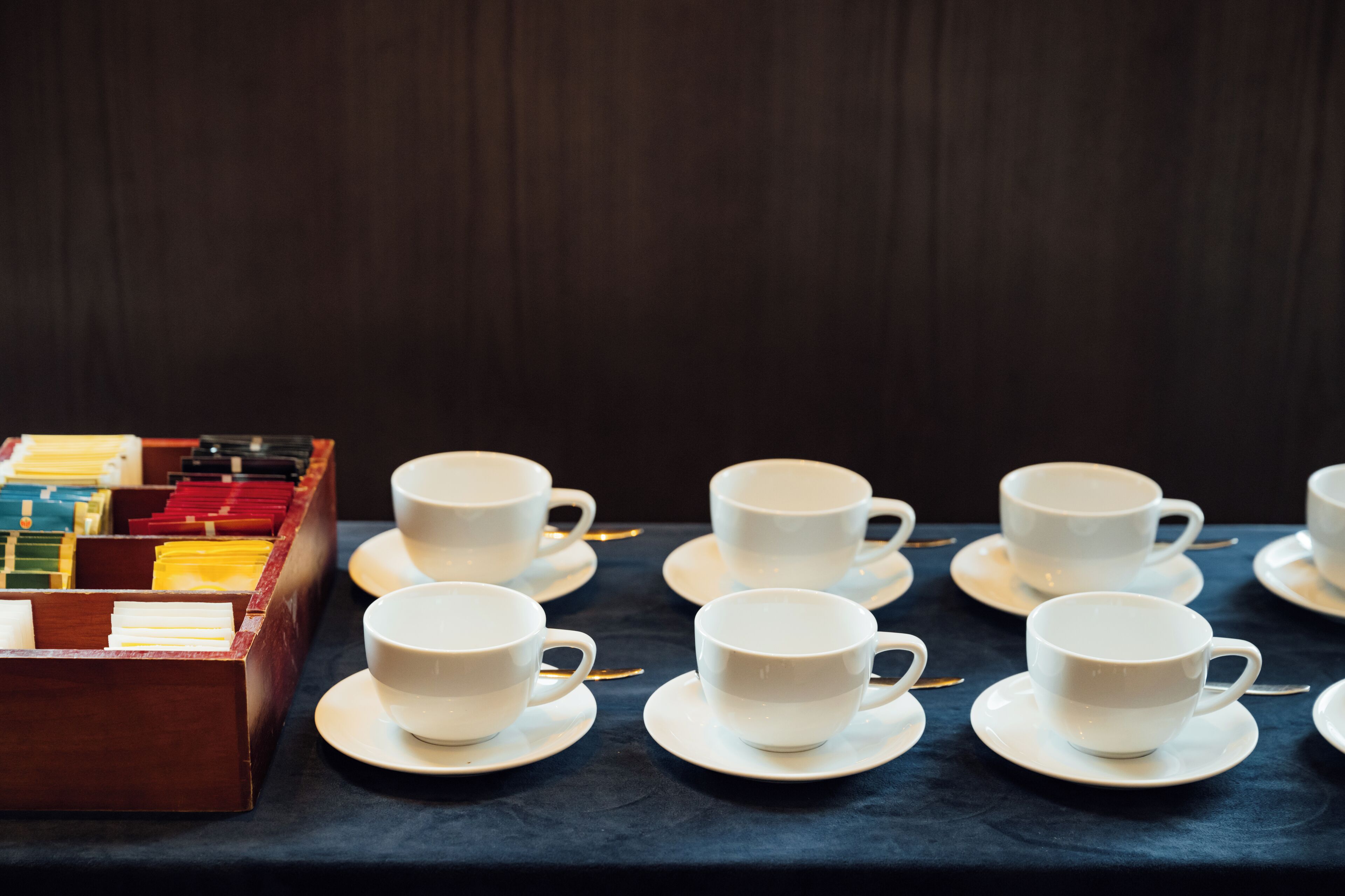 A table with white cups and saucers, arranged neatly on a dark tablecloth.