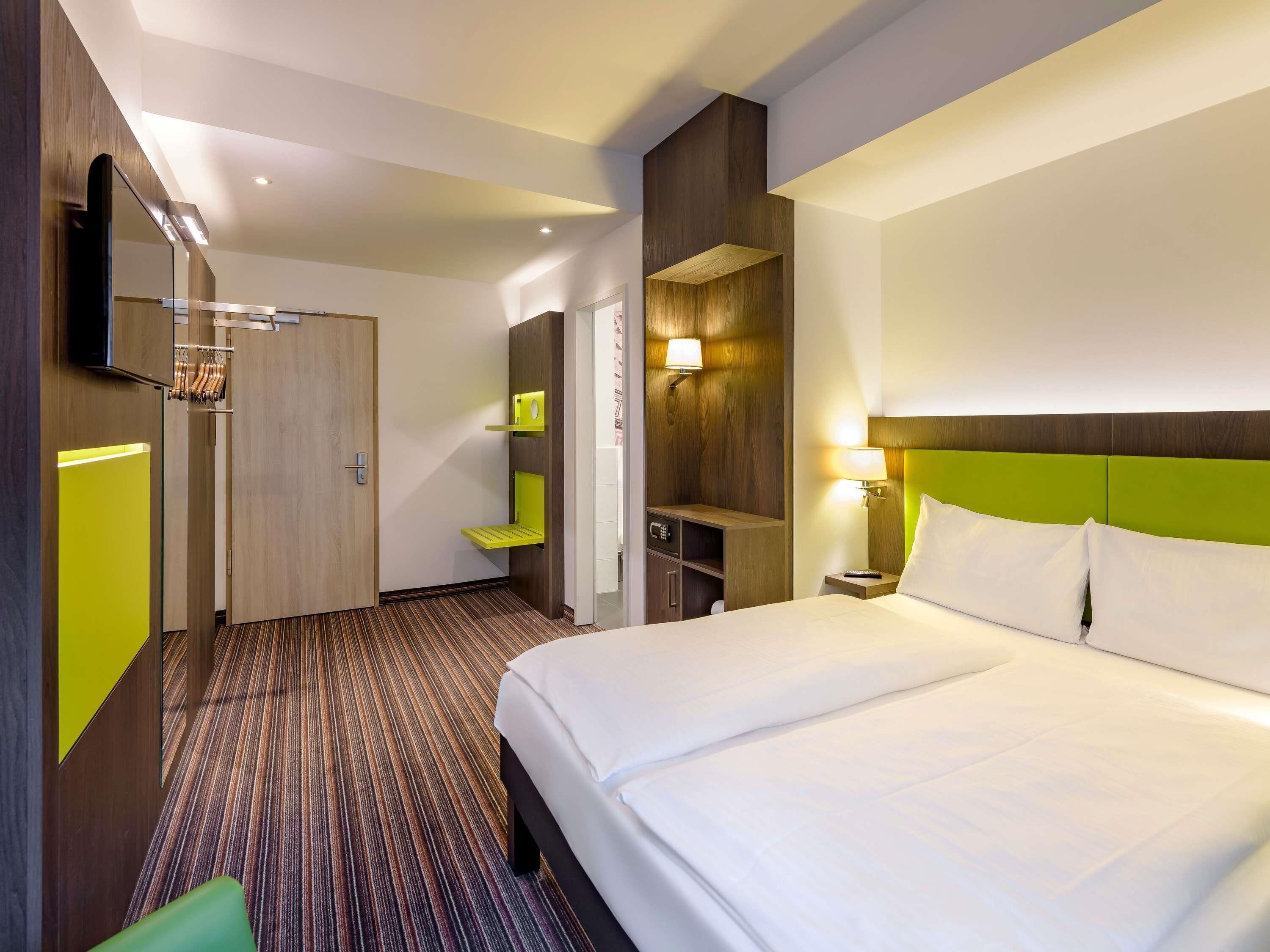 A hotel room with a bed, a desk, a chair, and a bathroom.