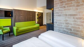 Una habitación de hotel moderna con un sofá verde, una cama, una lámpara colgante y una pared de ladrillo.
