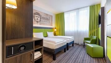 Habitación de hotel con dos camas, un mueble de madera con minibar, una silla verde y un ventanal con cortinas verdes.