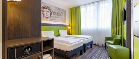 Habitación de hotel con dos camas, un mueble de madera con minibar, una silla verde y un ventanal con cortinas verdes.