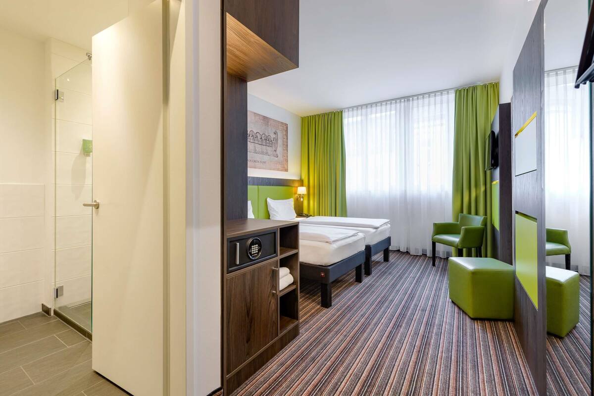 A hotel room with a bed, a desk, a chair, and a shower area.
