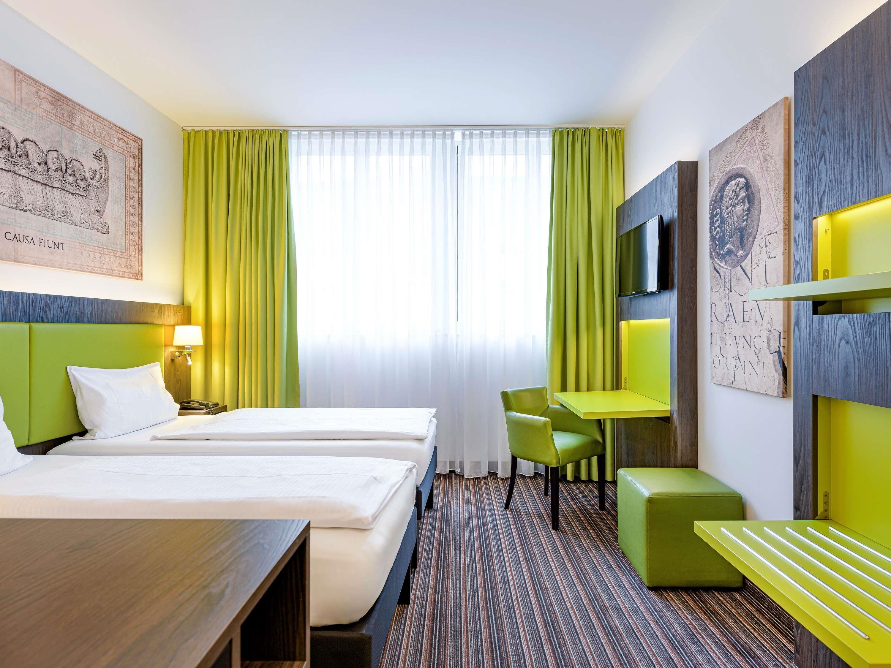 A hotel room with two beds, a desk, a chair, and a TV.