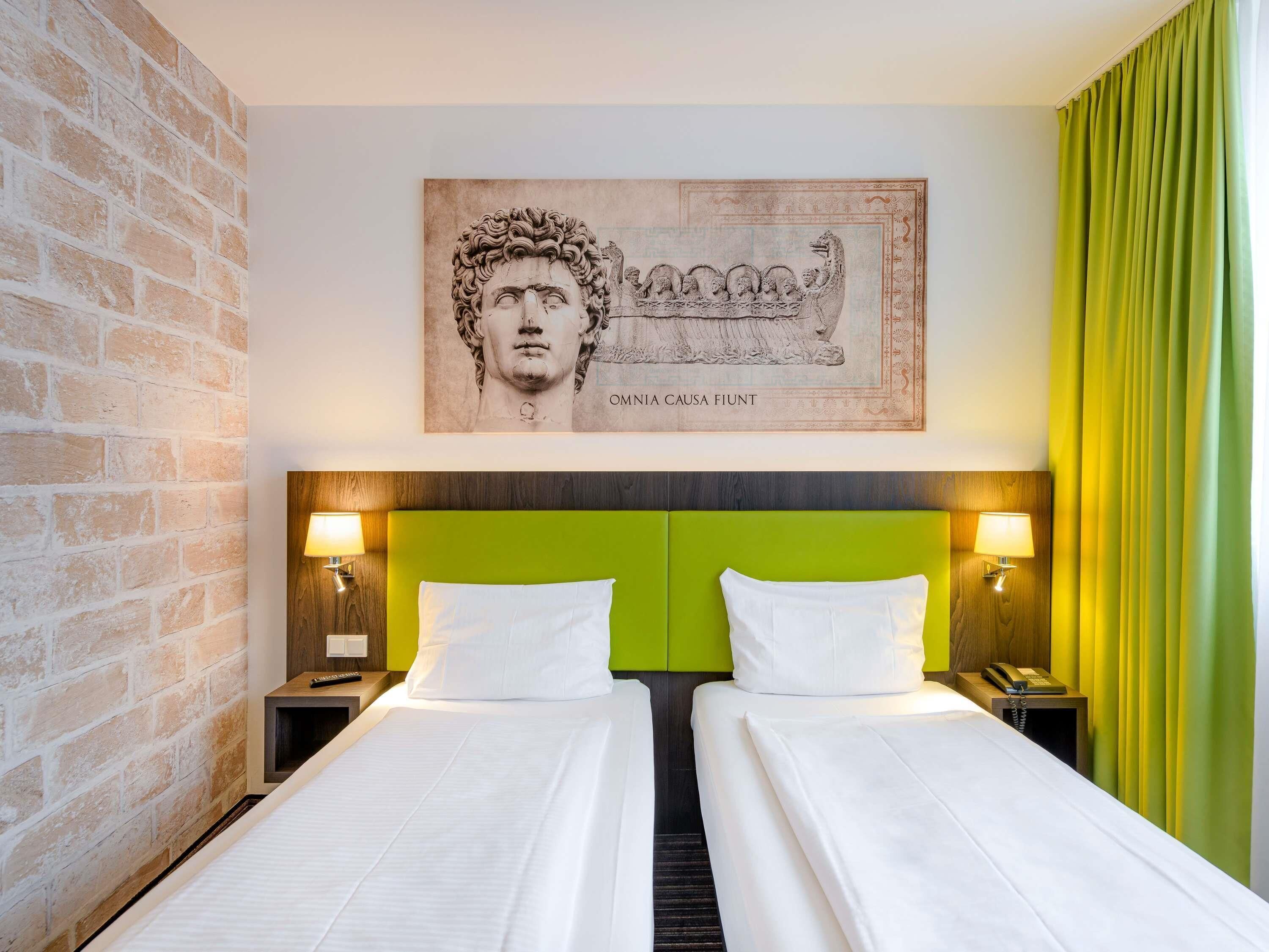 A hotel room with two beds, a brick wall, a green headboard, a framed artwork, and a telephone on the nightstand.