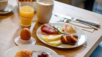 Uma mesa de café da manhã com pratos de comida, um copo de suco de laranja, uma xícara de café e um croissant.