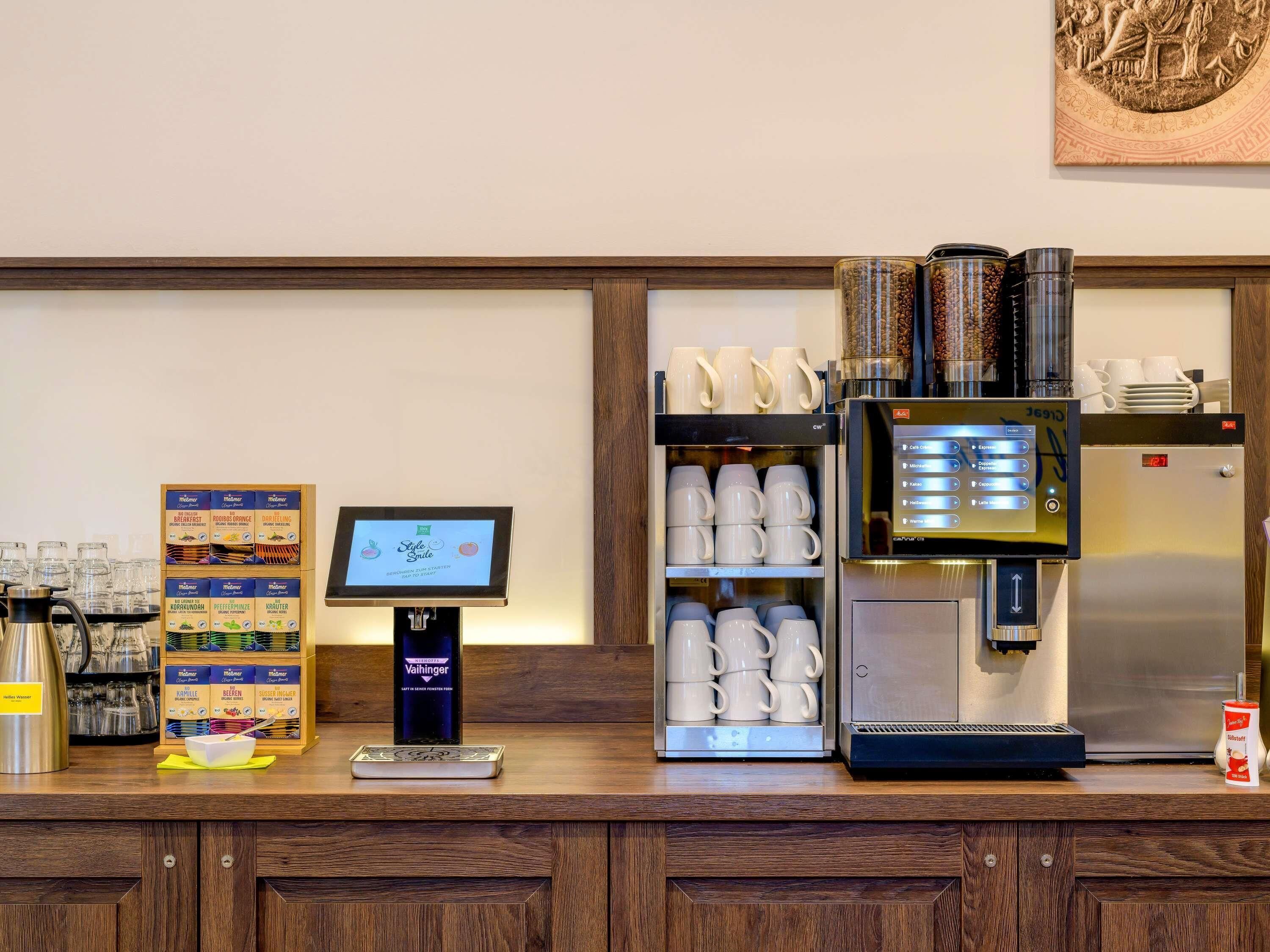 A coffee station with a digital menu, coffee machine, and a selection of mugs.