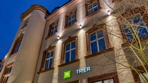 Un edificio de varios pisos con un estilo arquitectónico clásico, que presenta un letrero llamativo 'TRIER' y el logotipo 'ibis Styles'.