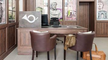 A wooden desk with a computer, two leather chairs, a brown leather bag, and framed artwork on the walls.