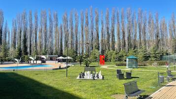 A park with a chessboard, benches, a pool, and tall trees.