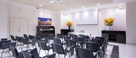A conference room with rows of chairs, a whiteboard, and two flower arrangements.