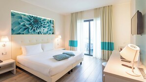 Habitación de hotel con una cama grande, lámparas de noche, un escritorio con lámpara, un televisor y una obra de arte floral de gran tamaño en la pared.