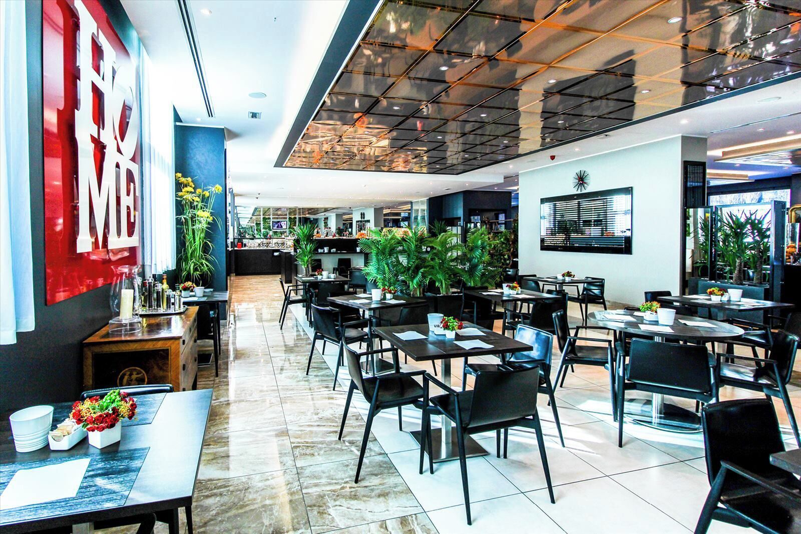A modern restaurant with multiple dining tables and chairs, a counter area, and potted plants.