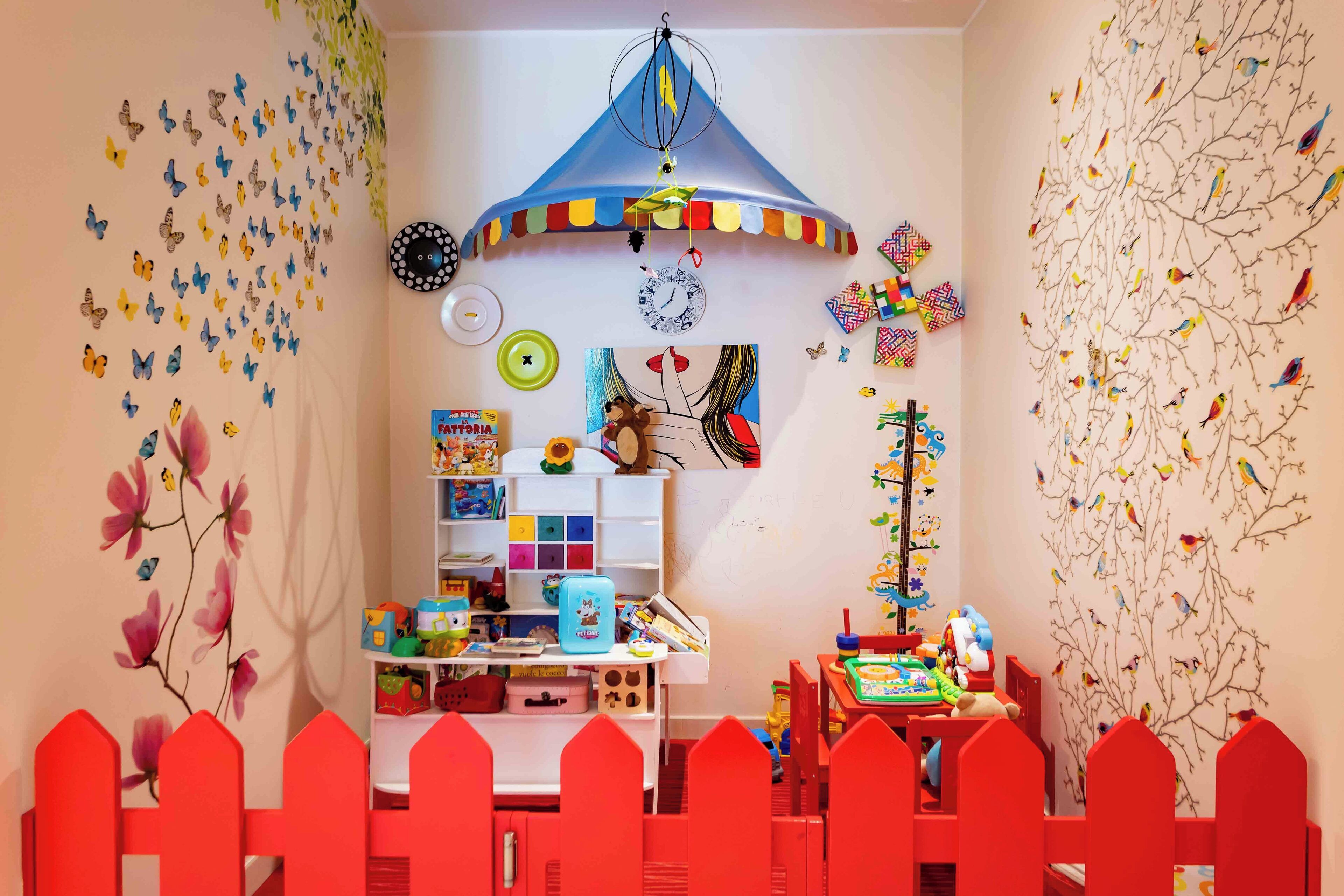 Un cuarto de juegos infantil con una alberca roja, un juguete colgante y un reloj de pared.