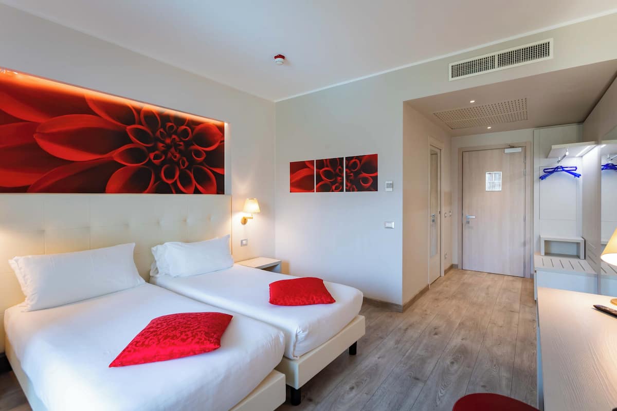 Une chambre d’hôtel avec deux lits, une grande œuvre d’art florale au mur et une salle de bain moderne dotée d’un miroir et d’un porte-serviettes.