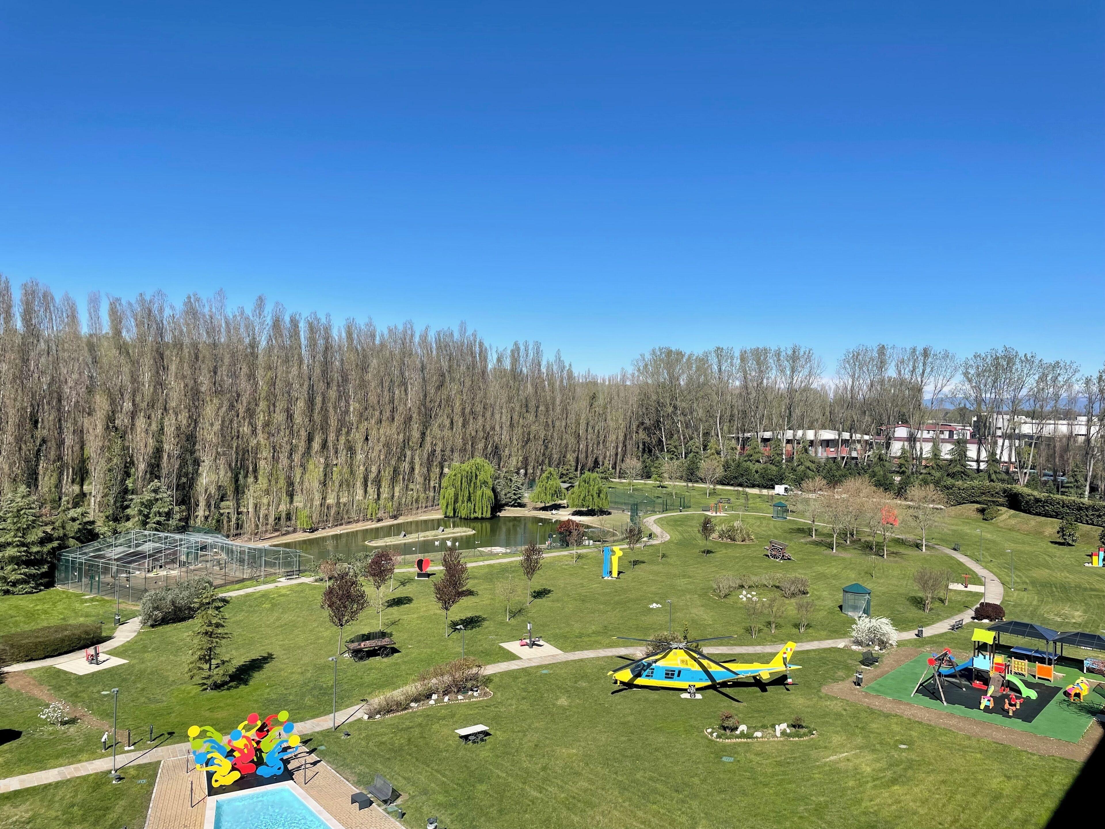 A park with a pond, playground, and a helicopter on the grass.