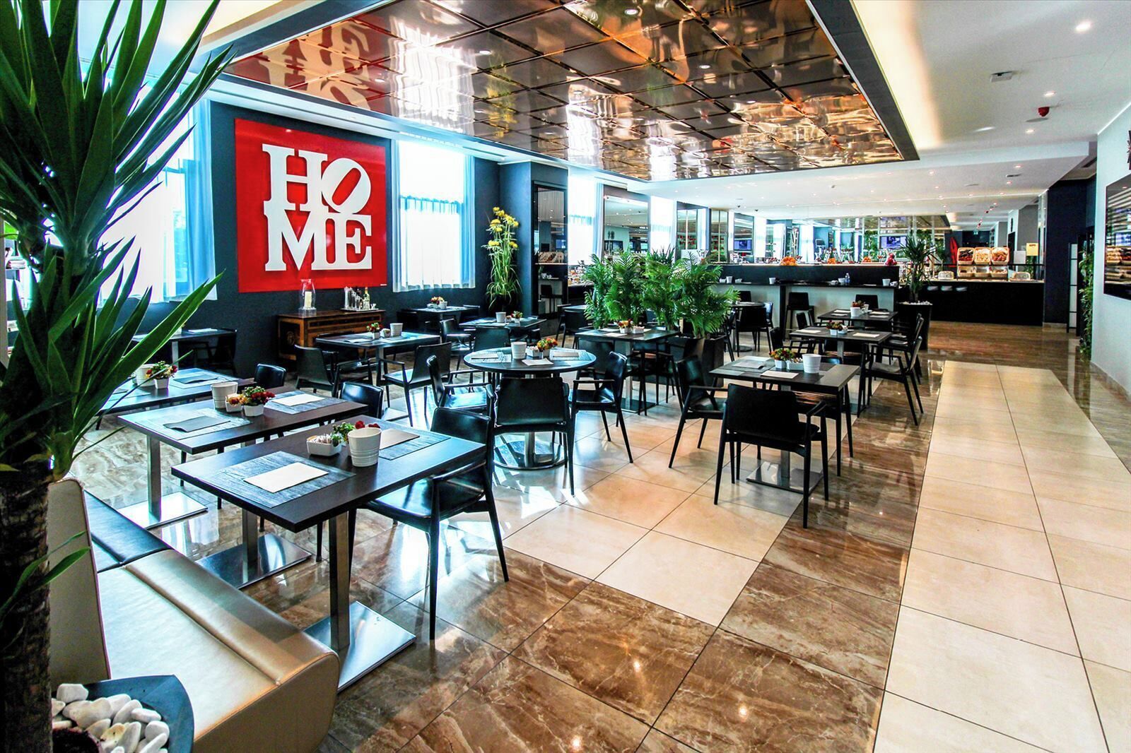 A modern hotel lobby with a 'HOME' sign, multiple seating areas, and a central bar.